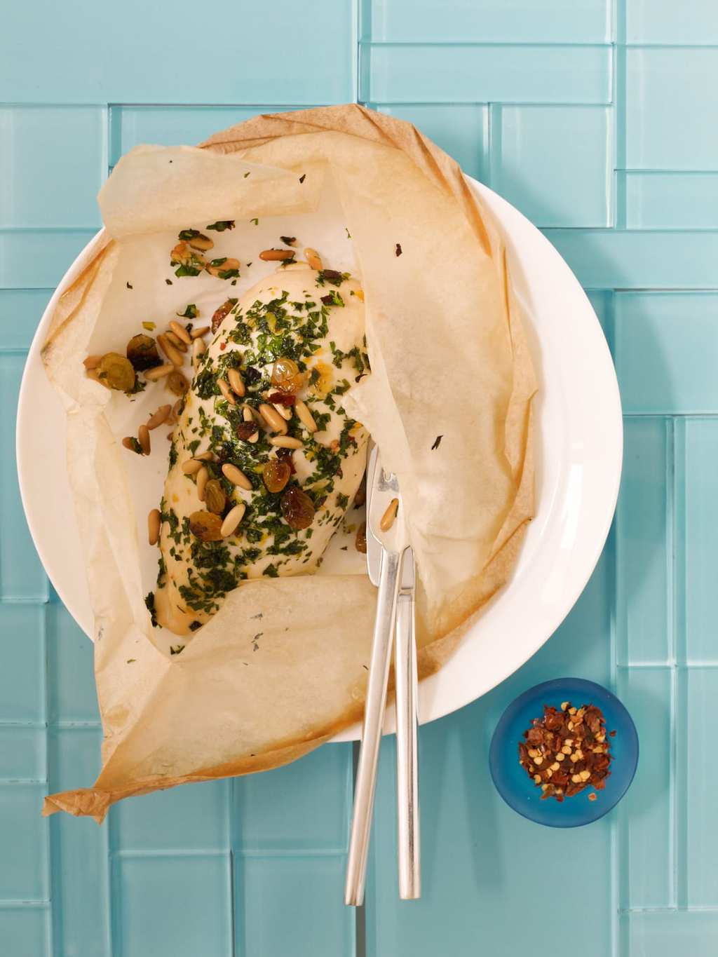 baked chicken in paper with raisins and pine nuts on blue tile
