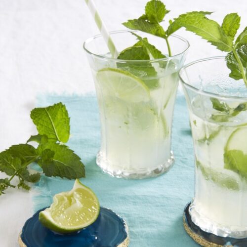 fresh mint limeade in clear glasses on blue towel with straws