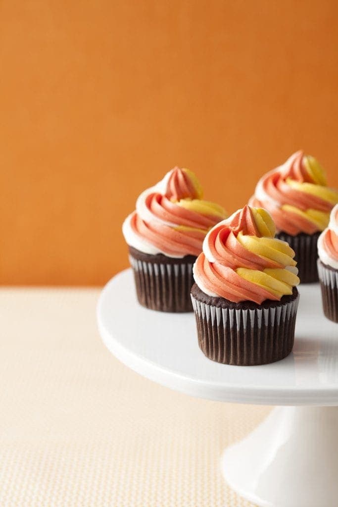Orange yellow and white twist frosting on top of chocolate cupcake on white cake stand