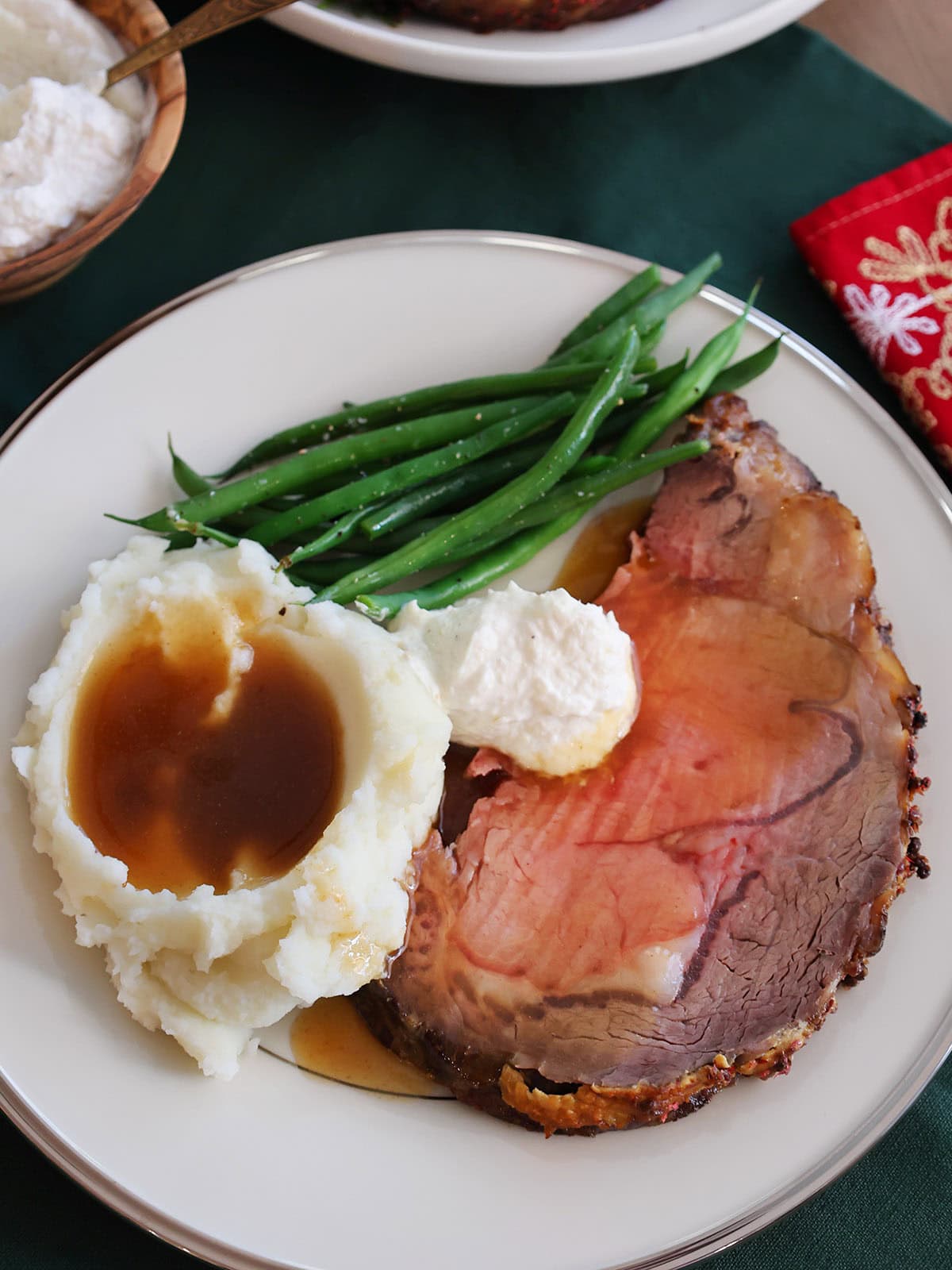 A slice of prime rib on a plate with mashed potatoes, green beans and horseradish.