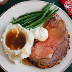 A slice of prime rib on a plate with mashed potatoes, green beans and horseradish.