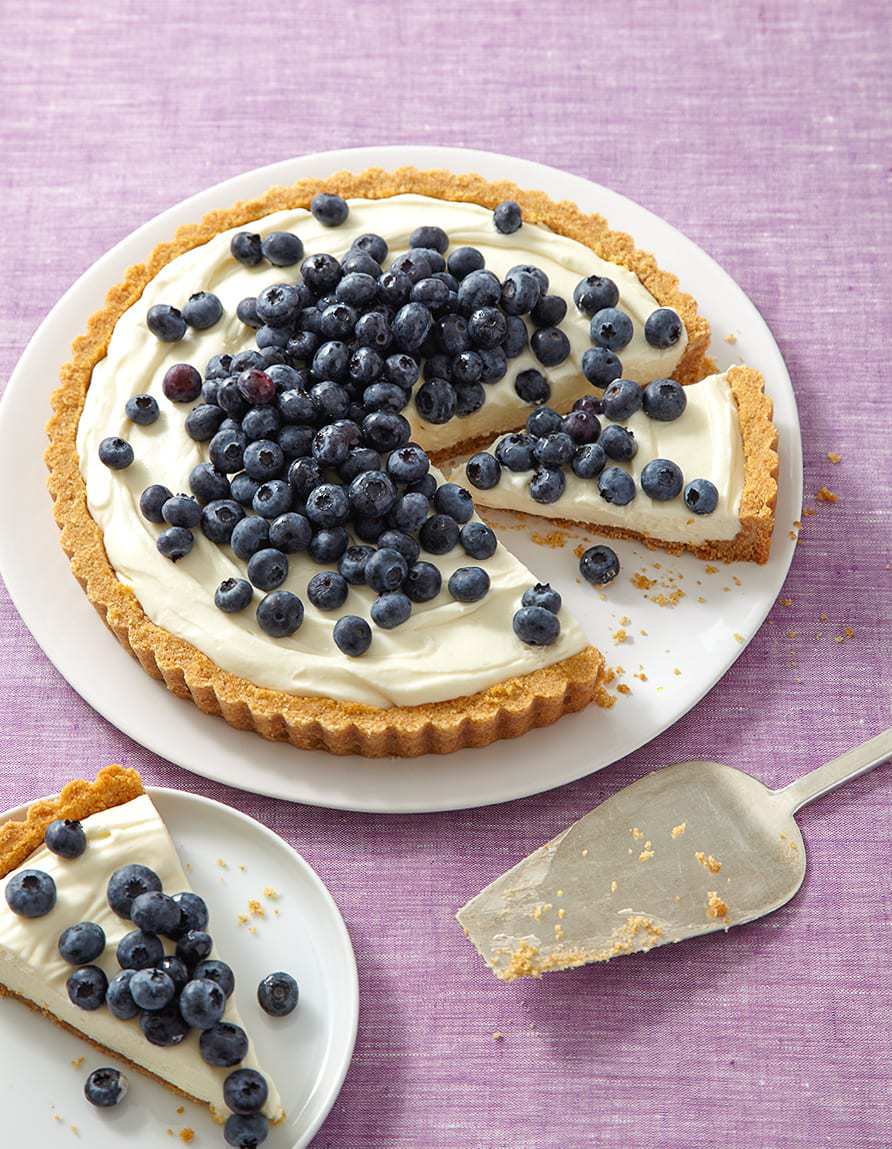 A simple no bake cheesecake topped with blueberries on a large plate, with a slice of cheesecake on a dessert plate next to it. 