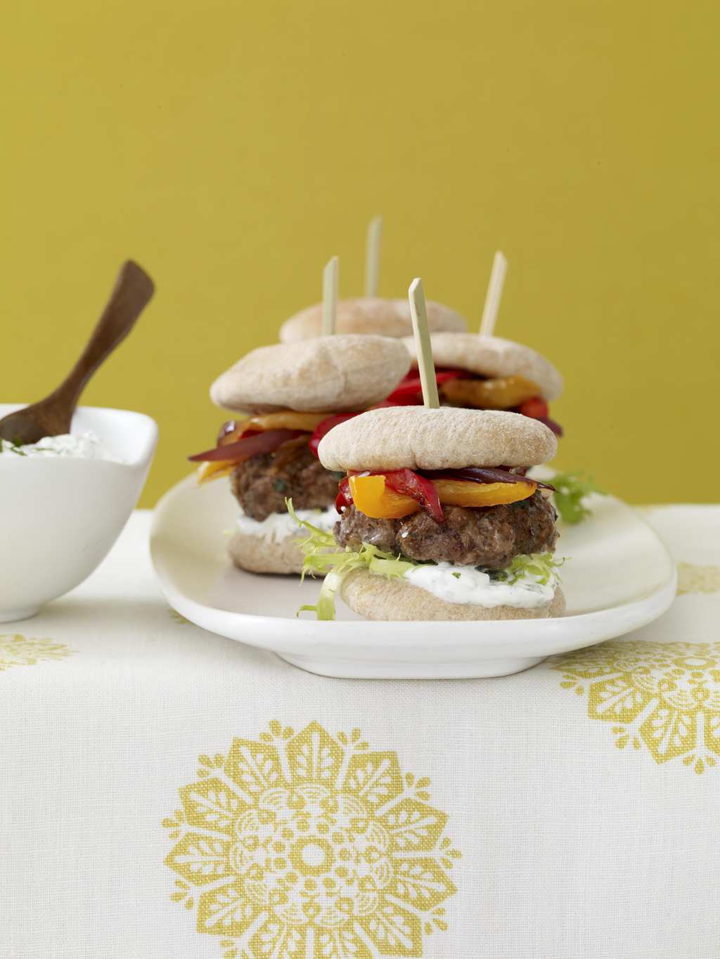 Mini burgers on white platter w yellow linen and background