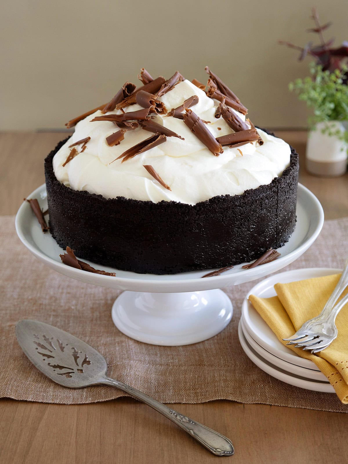 A ginger cheesecake on a white cake stand decorated with whipped cream and chocolate curls.