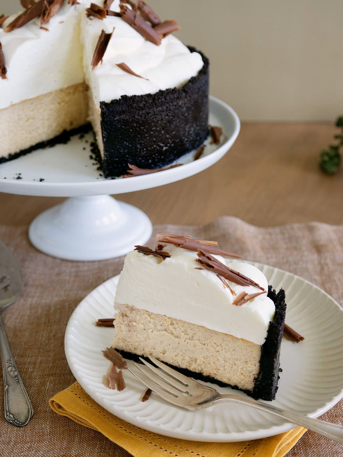 A slice of ginger cheesecake on a small white plate with the rest of the cheesecake in the background.
