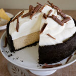 A ginger cheesecake on a white cake stand with a slice removed to see layers.