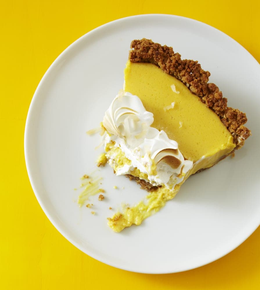 Overhead view of a slice of coconut mango custard pie on a white pate. A generous bite has already been taken from the slice. 