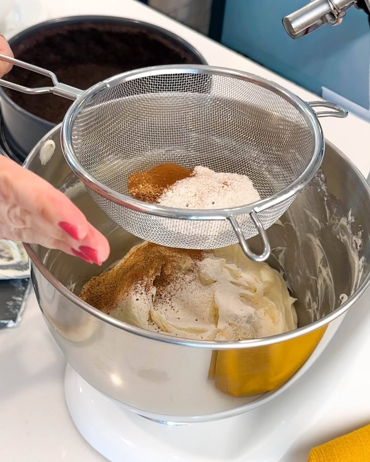 Sifting flour and ground spices into cheesecake filling mixture.