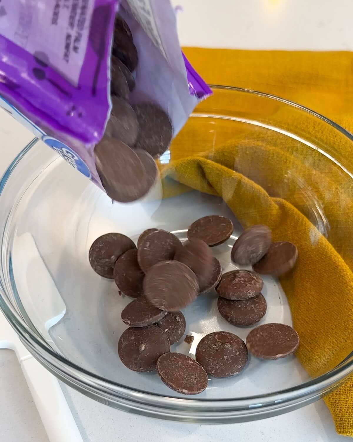 Chocolate wafers being poured into a glass bowl.