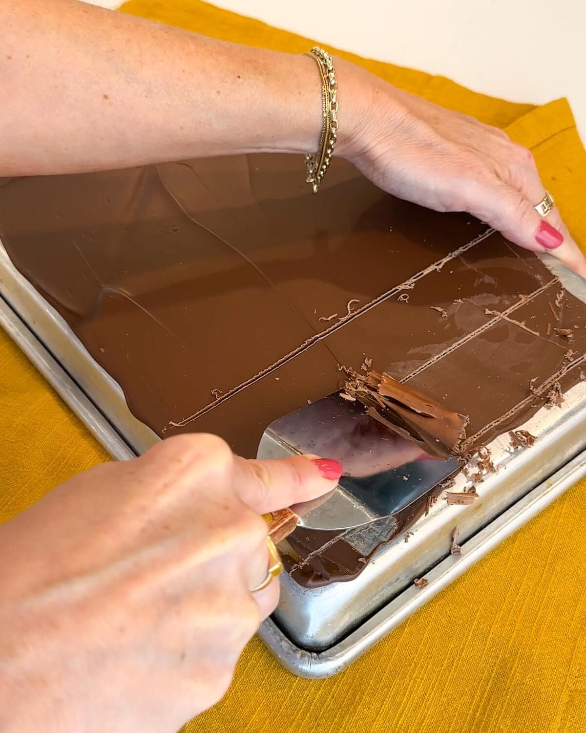 Using a spatula to scrape chocolate off a pan into curls.