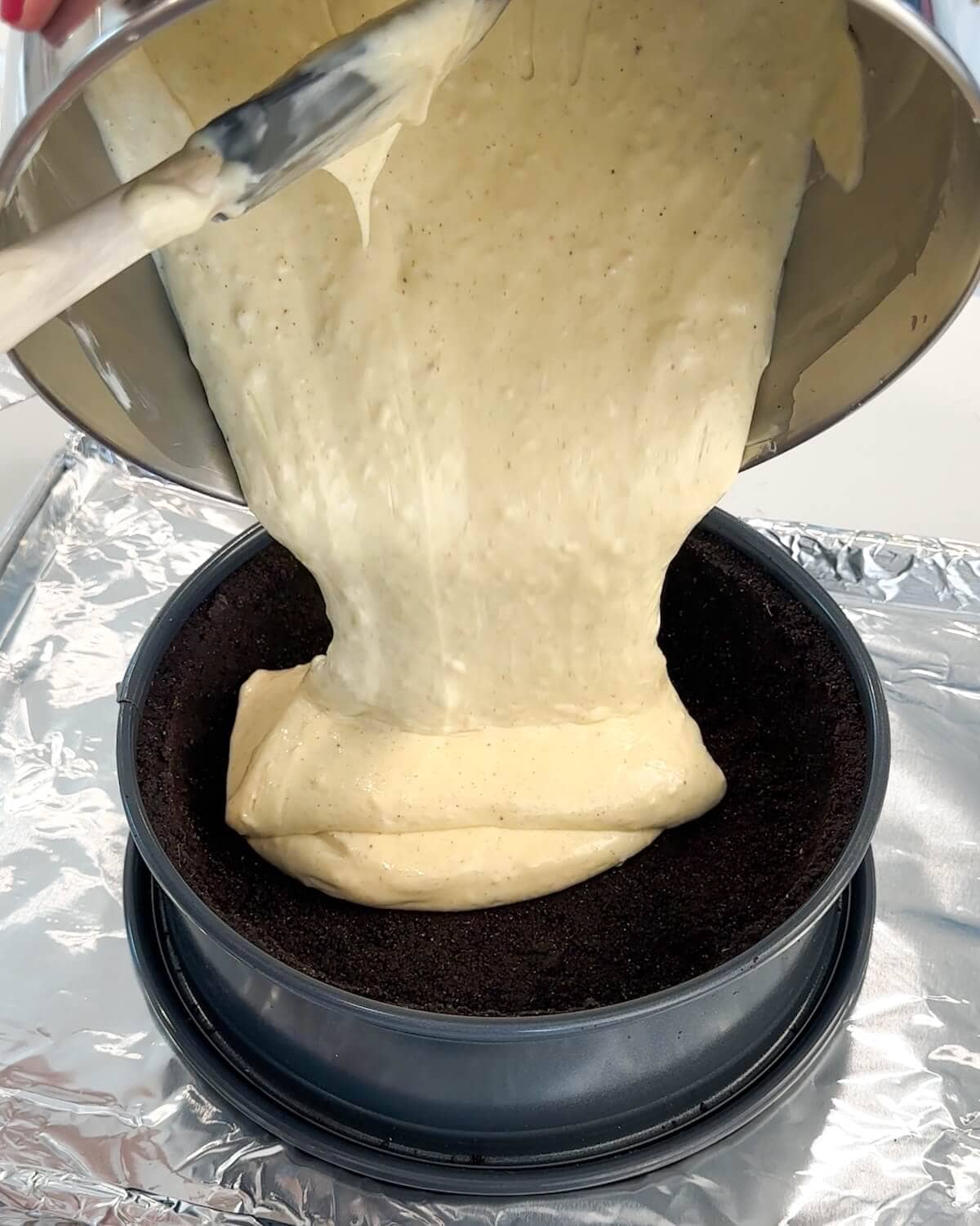 Pouring ginger cheesecake filling into a springform pan lined with chocolate cookie crust.