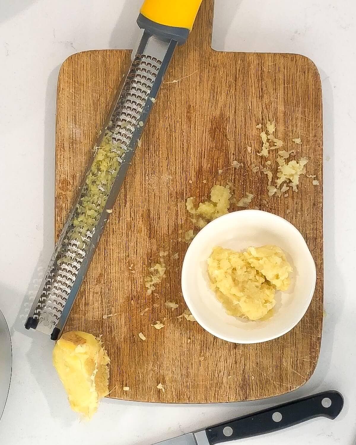Grated fresh ginger on a cutting board next to a microplane.