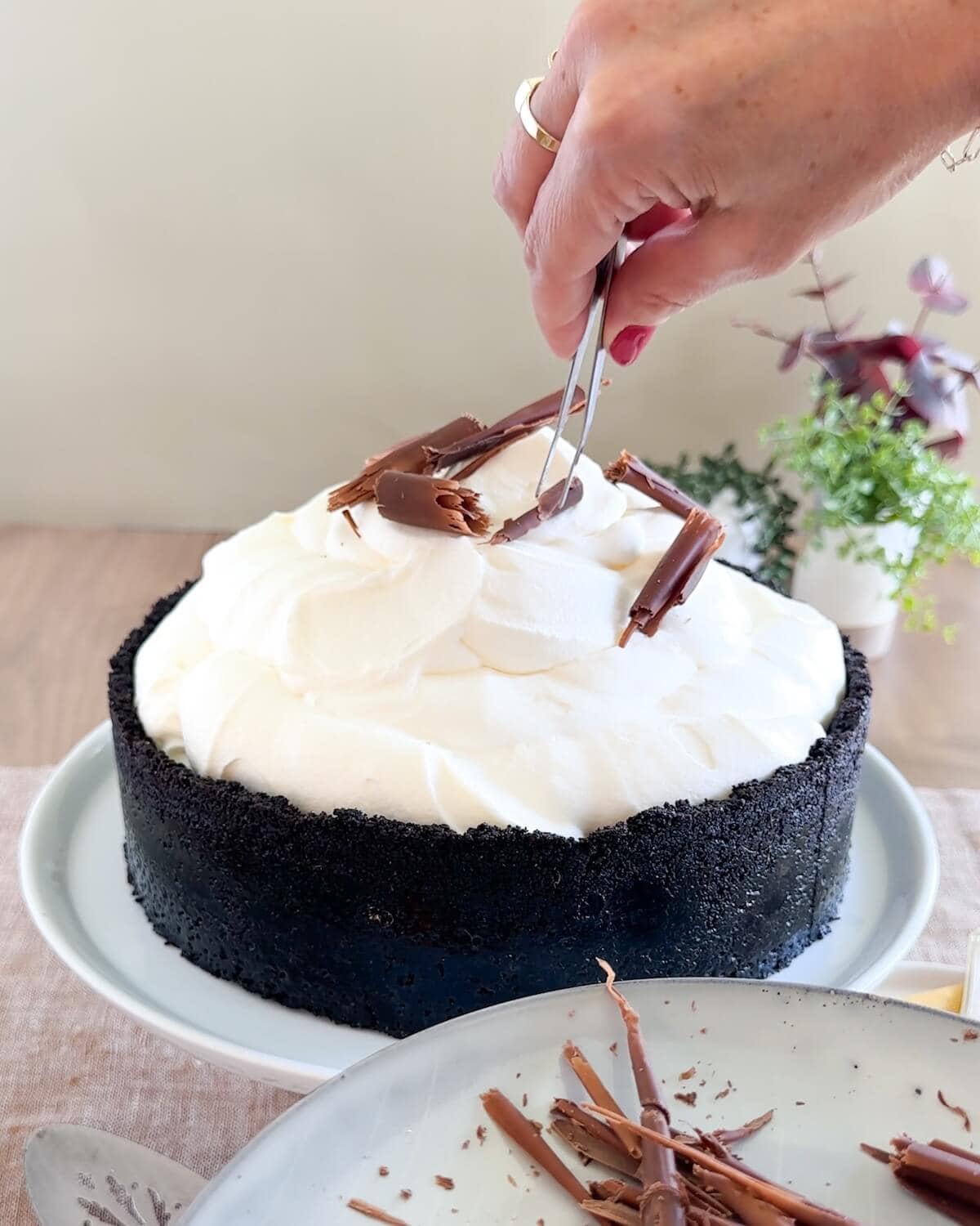 Using tweezers to place chocolate curls on top of a cheesecake.