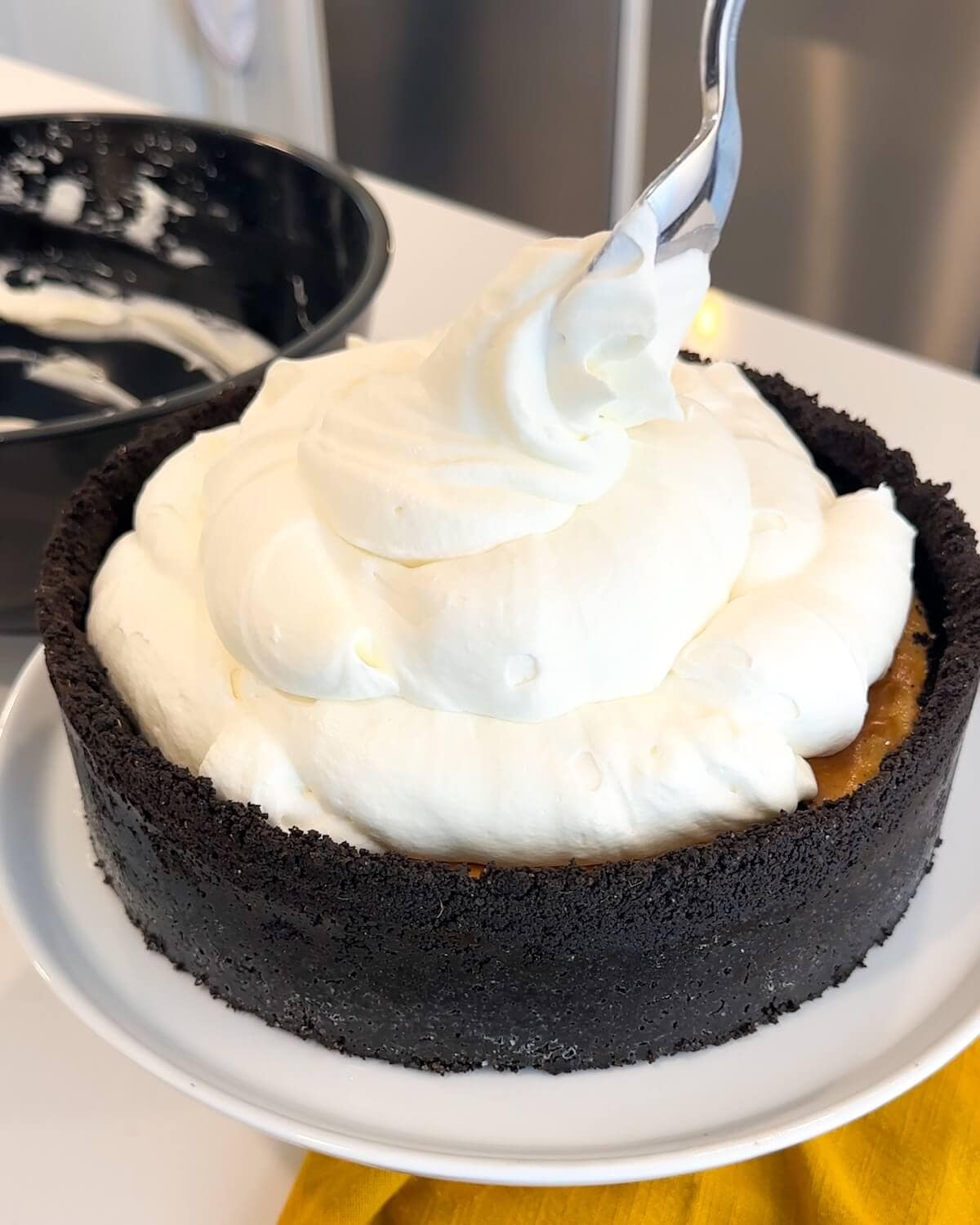 Piling whipped cream on top of a ginger cheesecake.
