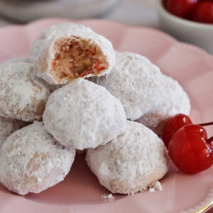 A pile of cherry almond cookies on a pink plate with a bite taken out of top cookie.
