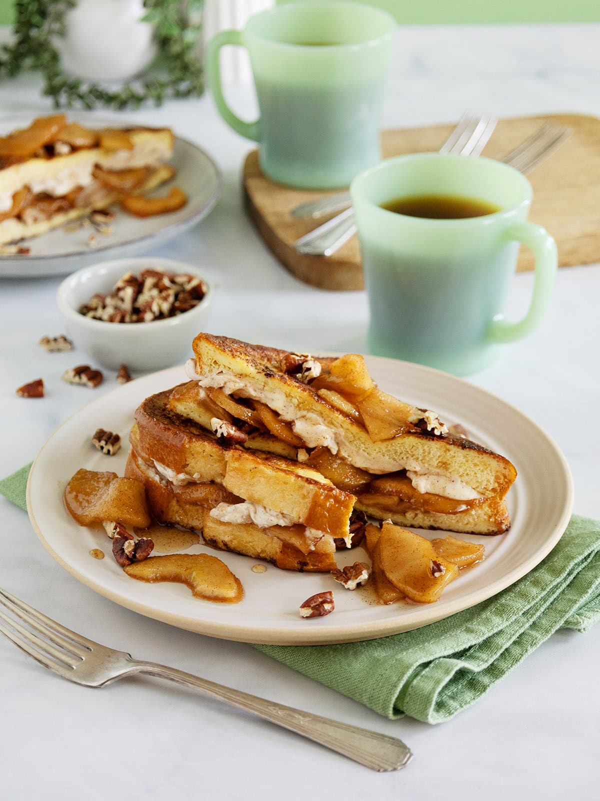 Apple French toast on a plate next to a green mug and green napkin.