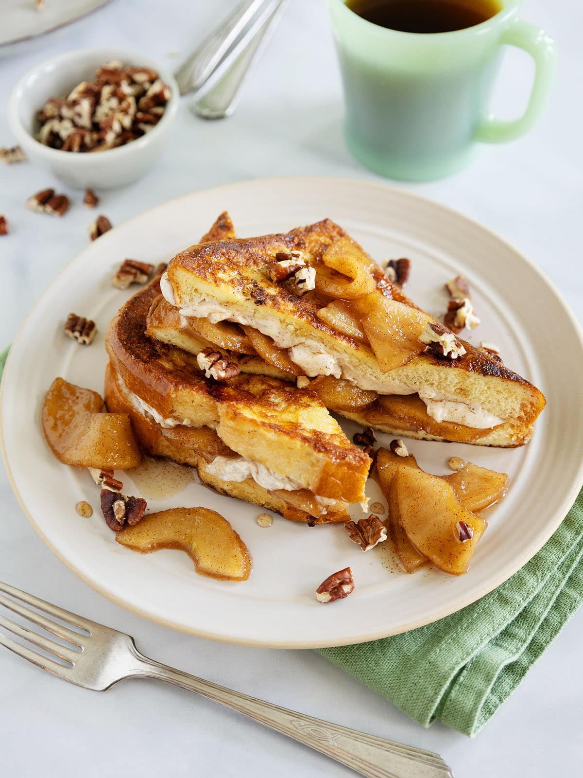 Apple French toast on a plate next to a green mug and green napkin.