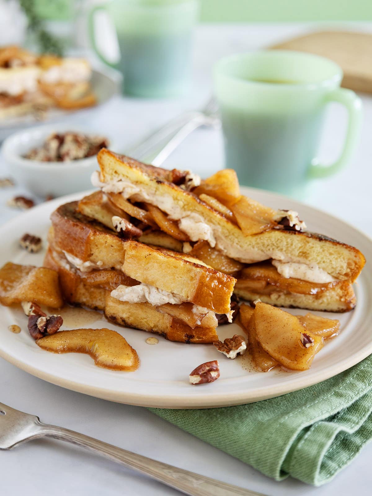 Apple French toast on a plate next to a green mug and green napkin.