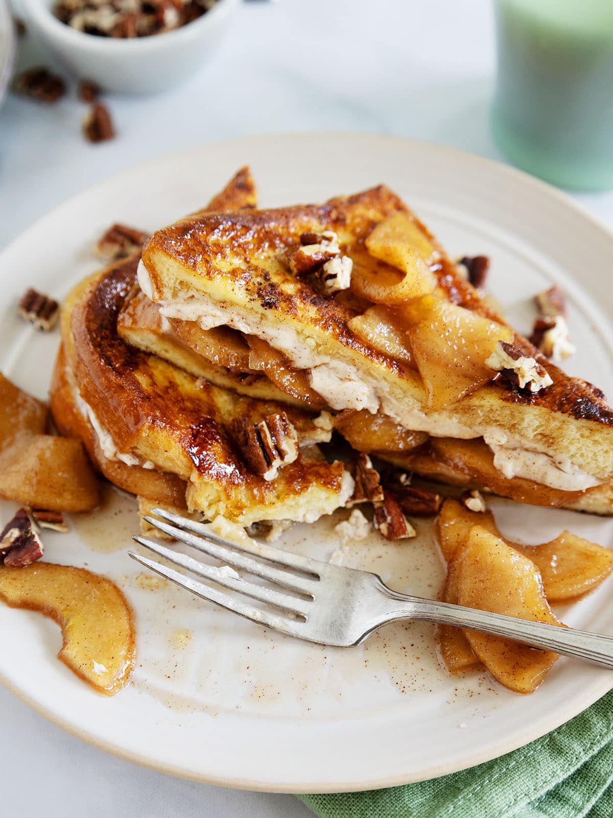 Apple French toast on a plate with a fork on it next to a green mug and green napkin.