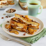Apple and cream cheese stuffed French toast on white plate ready to serve.