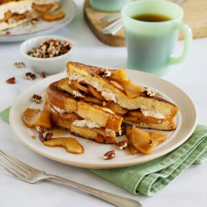 Apple French toast on a plate next to a green mug and green napkin.