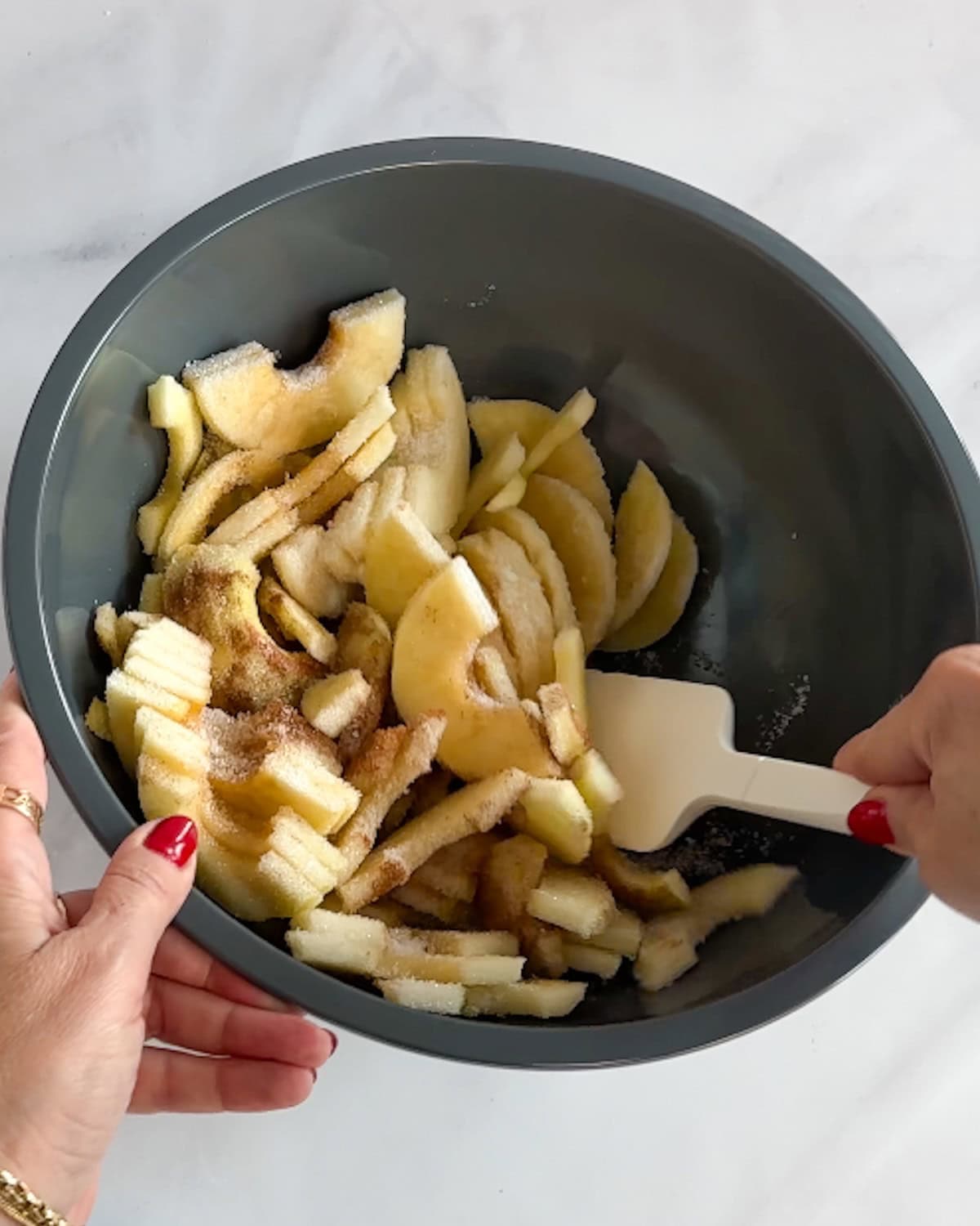 Mixing sliced apples in a bowl with sugar and cinnamon.