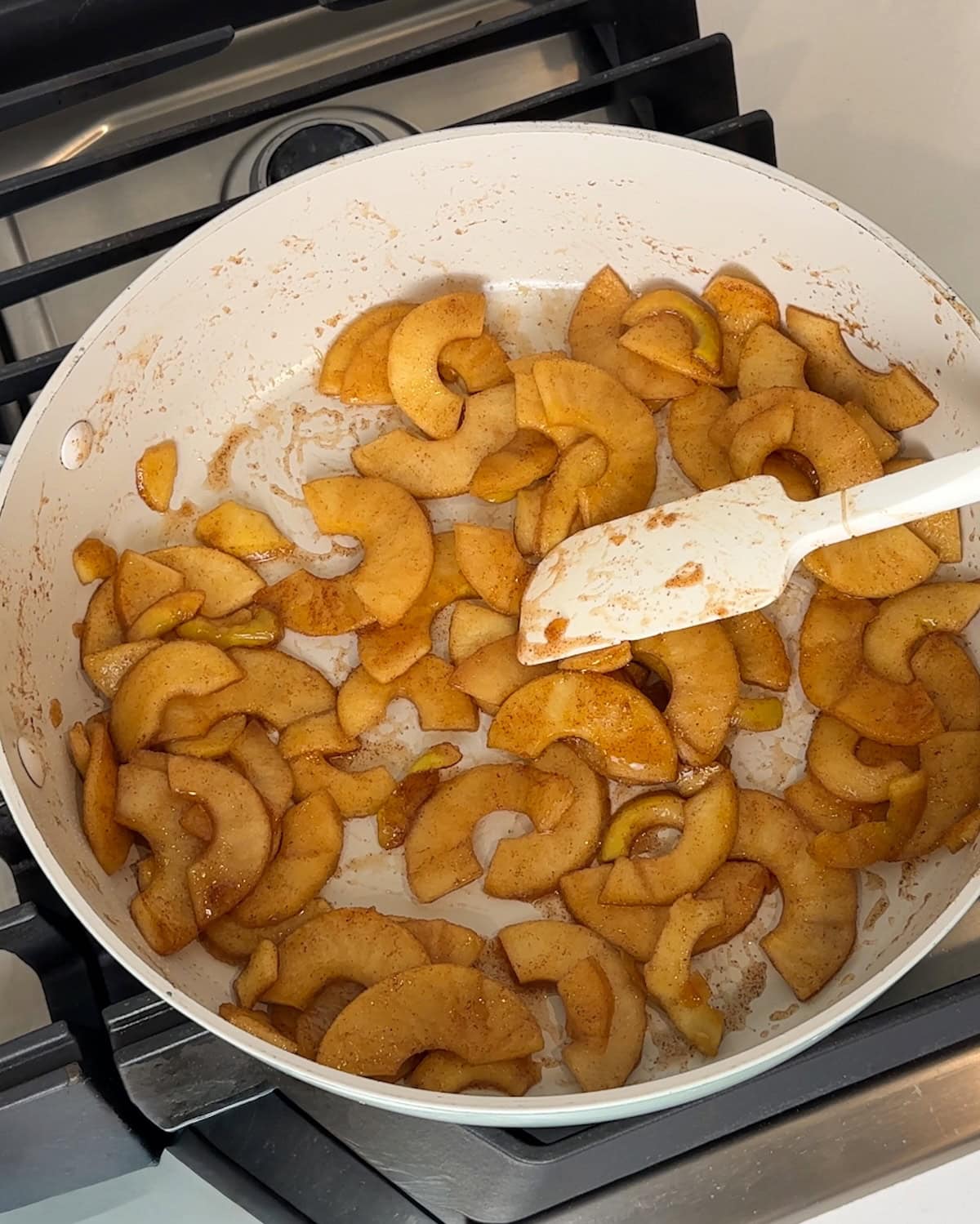 Stewed apples in a skillet being stirred with a spatula.