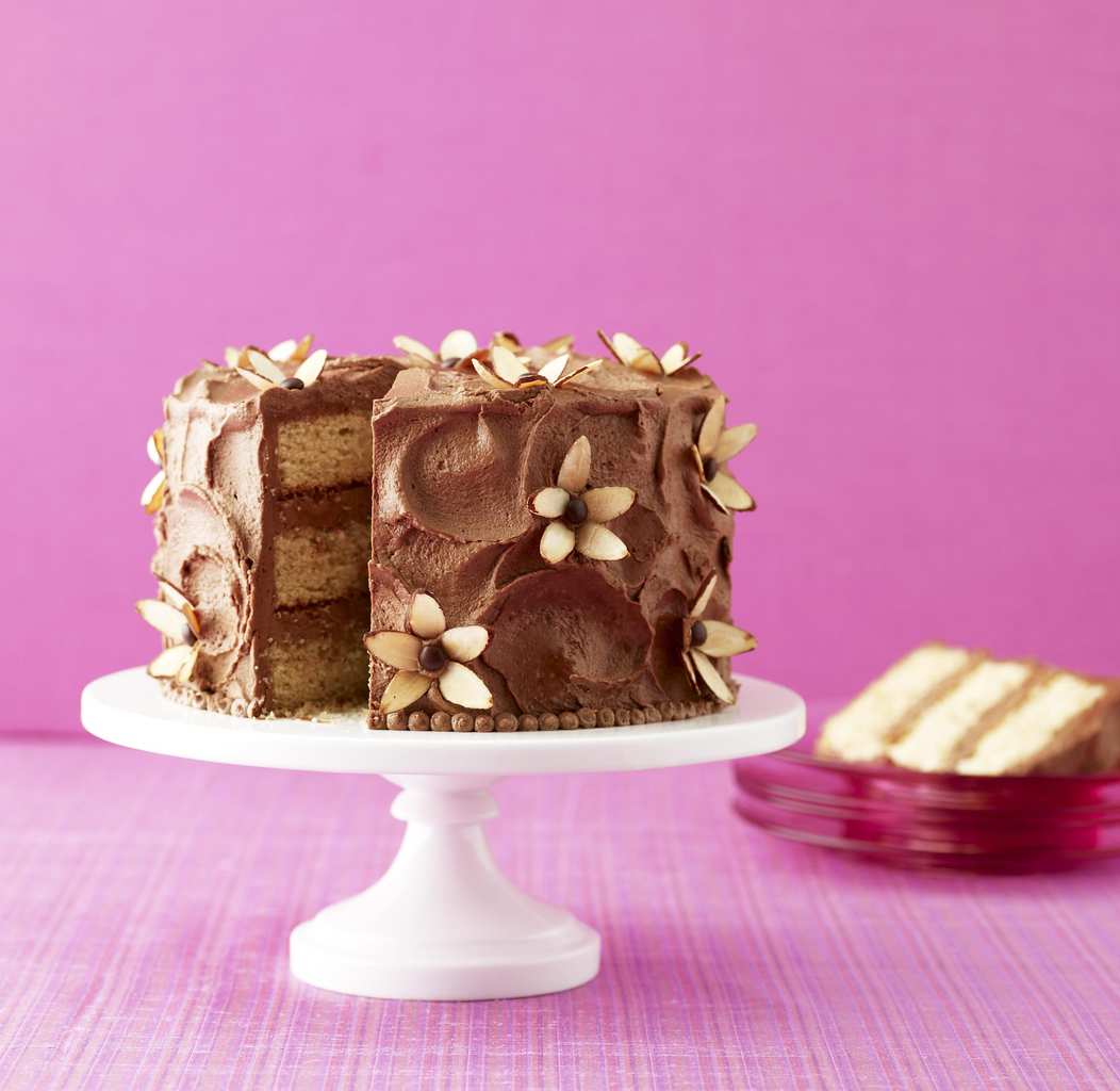 A chocolate almond cake topped with homemade chocolate frosting on a cake pedestal.  