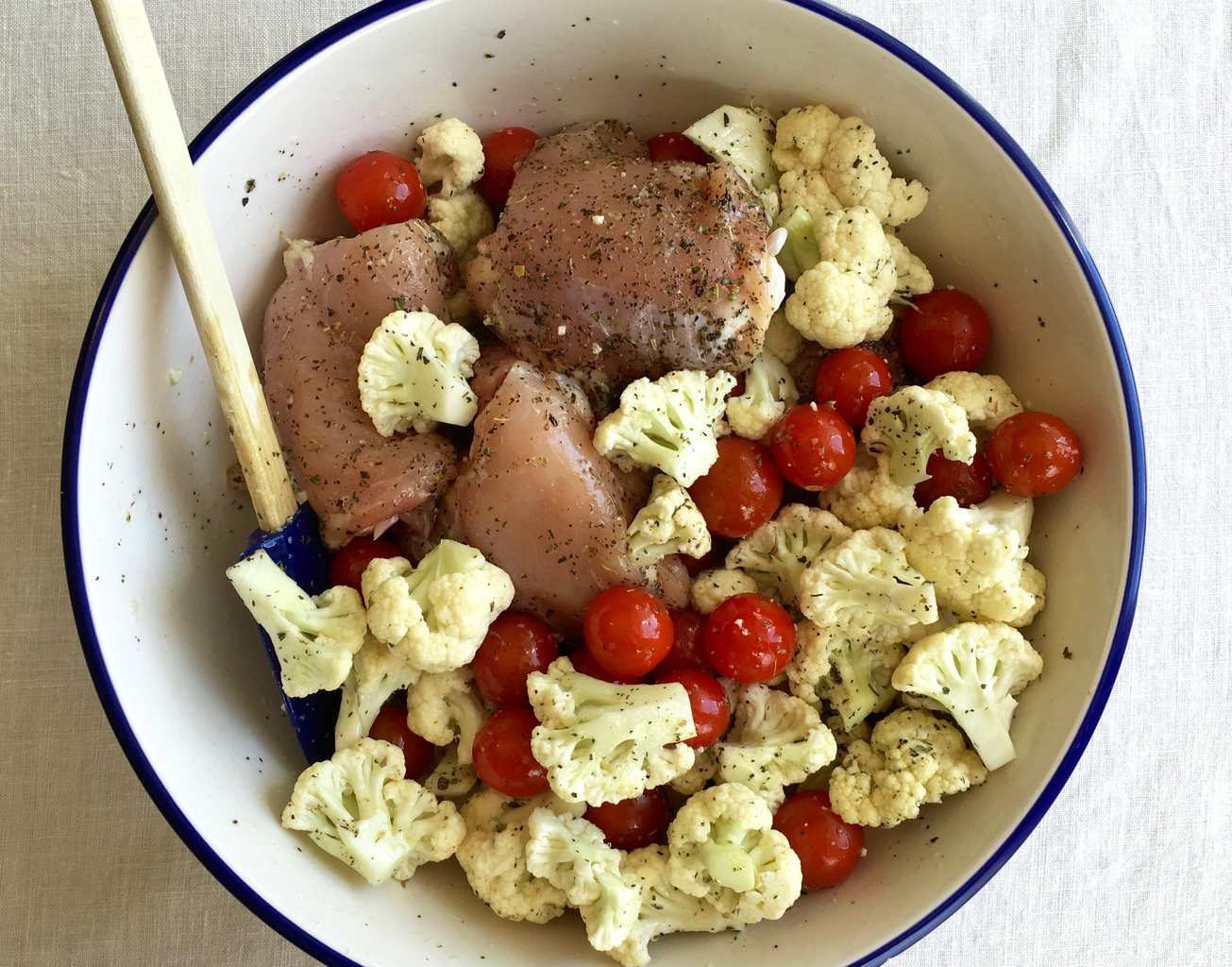 Raw chicken thighs, cauliflower, and tomatoes in a large bowl. 
