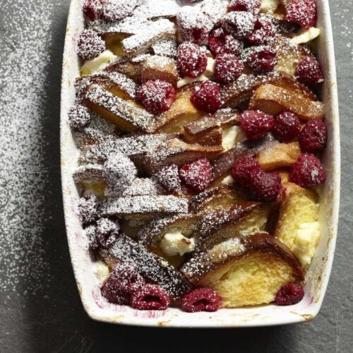 Raspberry french toast strata in white rectangle baking dish with powdered sugar