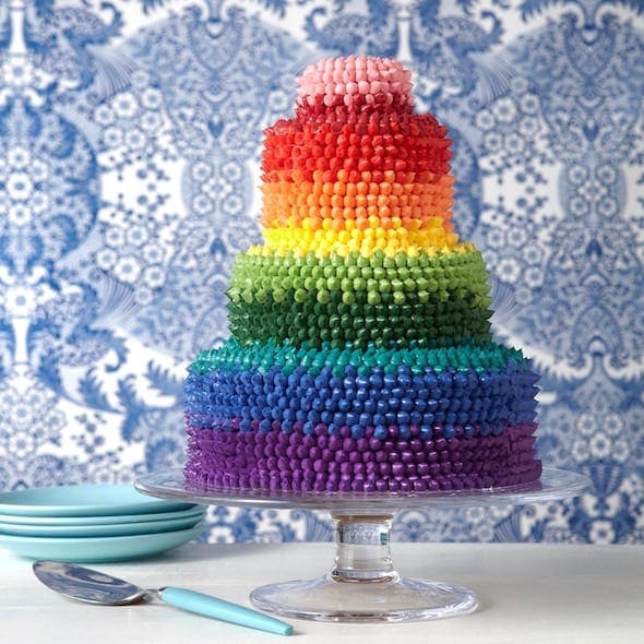 Party Rainbow cake on clear glass cake plate with blue floral background