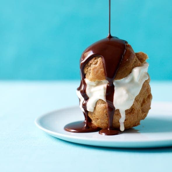 cream puff filled with ice cream in a plate with dripping hot fudge sauce.