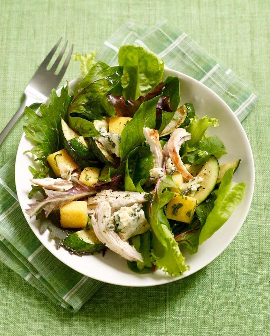 Warm Polenta Zucchini Salad in white bowl on green background.