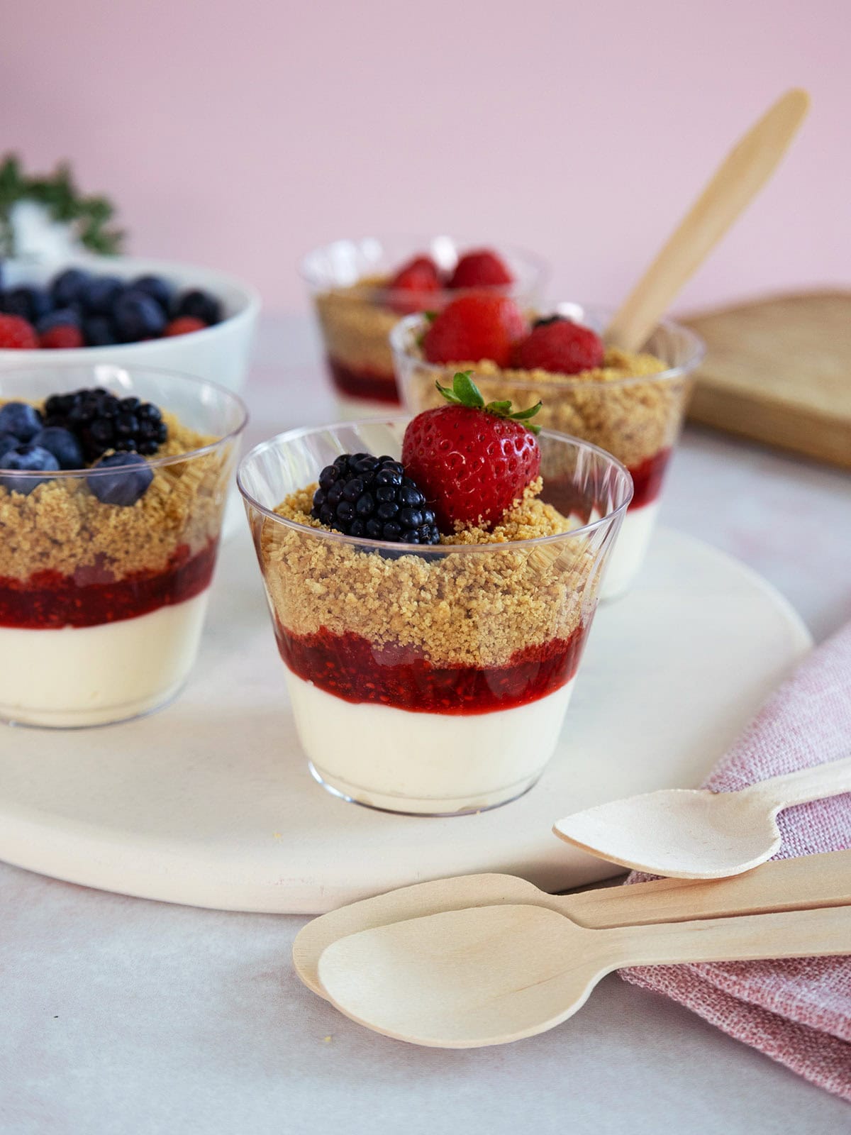 Mini cheesecakes in plastic cups with fruit on top.