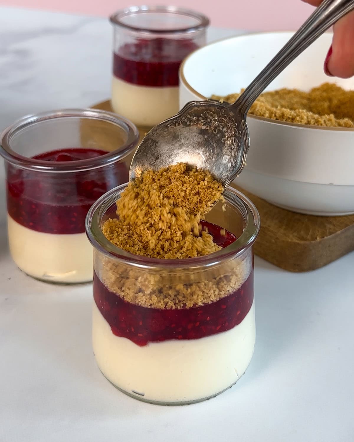 Spooning graham cracker crust crumbles on to the top of mini cheesecakes.