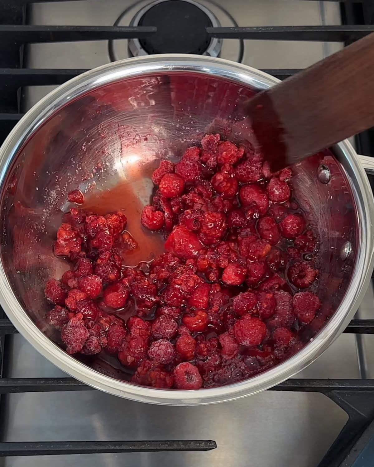 Stirring raspberries and sugar in a small saucepan.