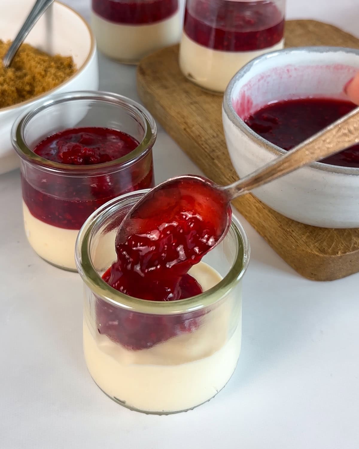 Spooning raspberry sauce over chilled no-bake cheesecake in a jar.