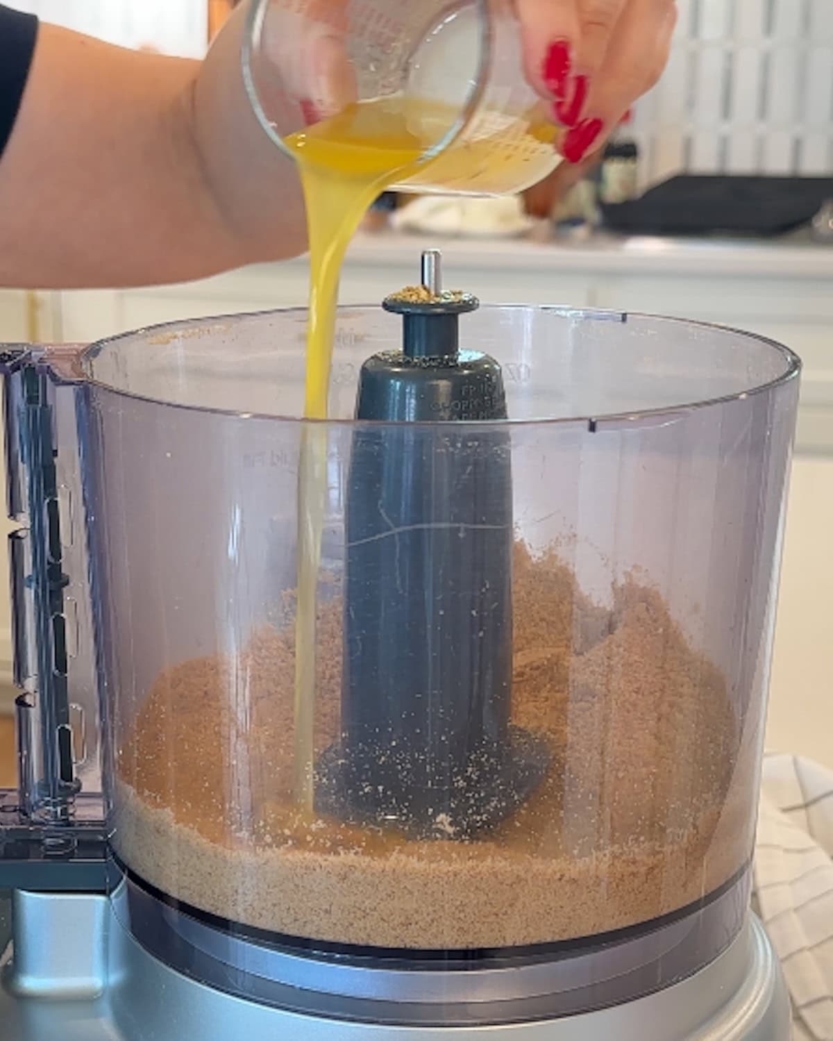 Pouring melted butter into graham cracker crumbs in a food processor.