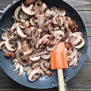 Mushrooms and onions being sautéed in a non-stick pan