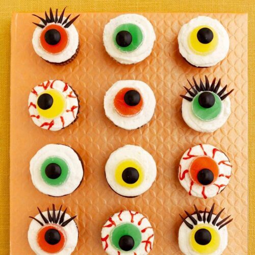 One dozen Eerie Eyeball Cupcakes on orange surface