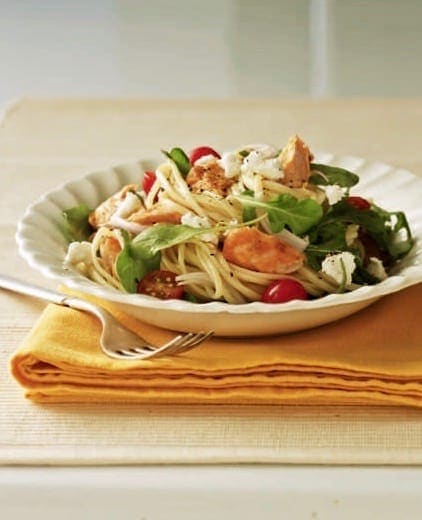 Warm salmon and arugula pasta salad in white bowl on yellow napkin