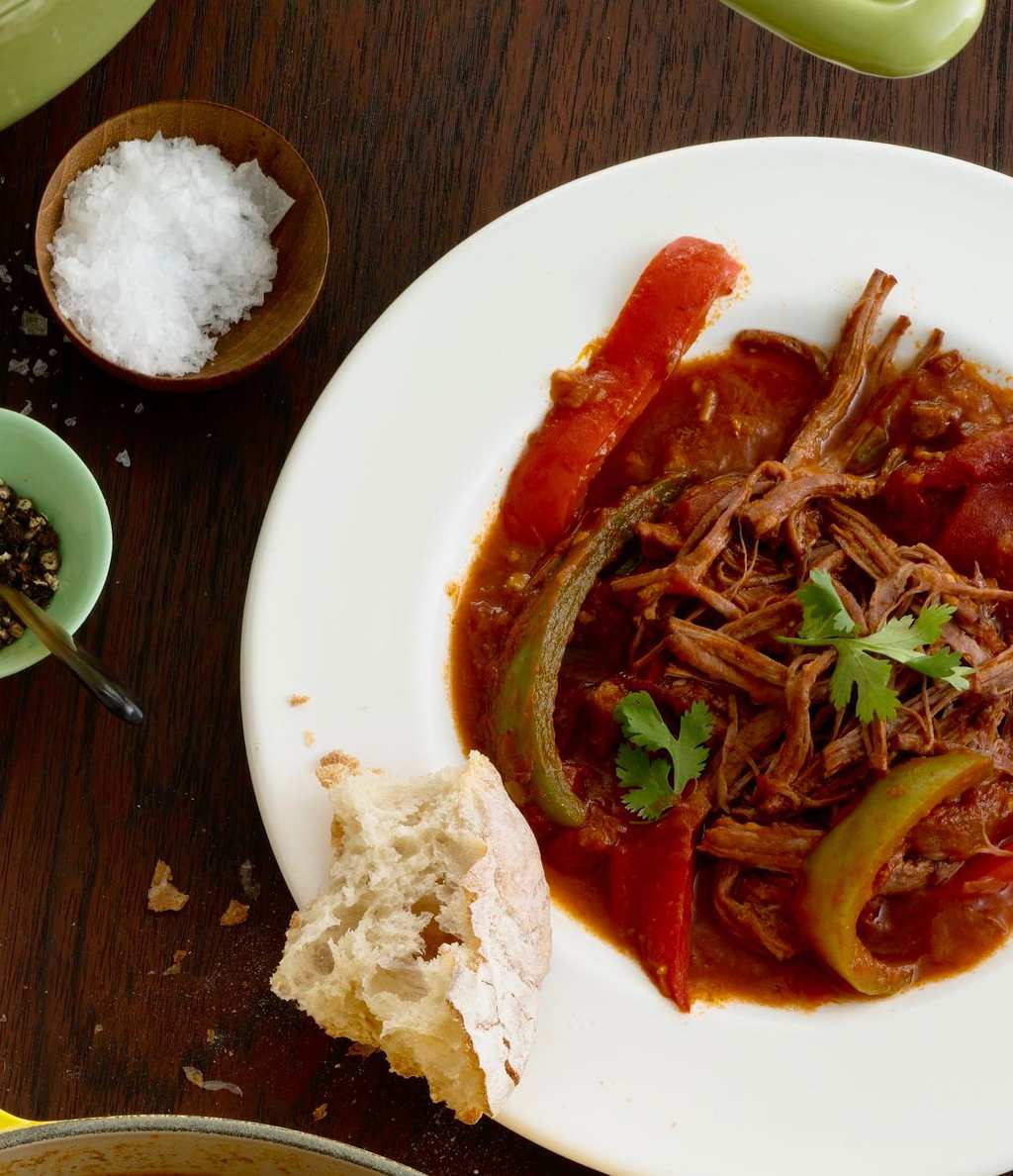 Ropa Vieja in white bowl with bread, salt and pepper on wooden table