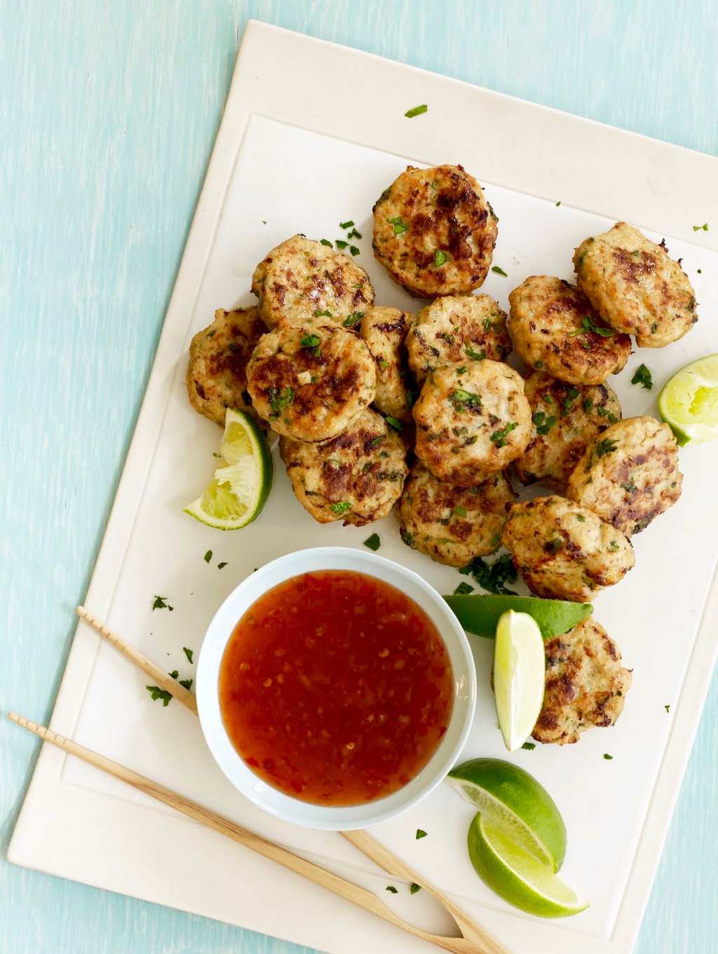 Ginger Thai Chicken Patties with sauce, limes and chopsticks overhead on white try and green background