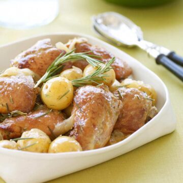 Slow cooker honey rosemary chicken in white serving dish on yellow surface