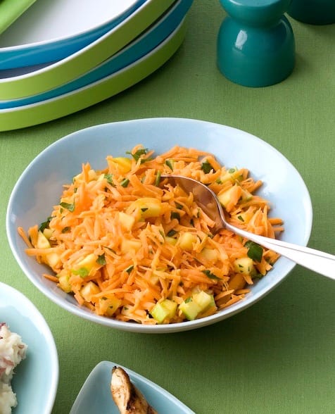 Shredded Carrot Salad with Apple and Lime in blue bowl with spoon on green background
