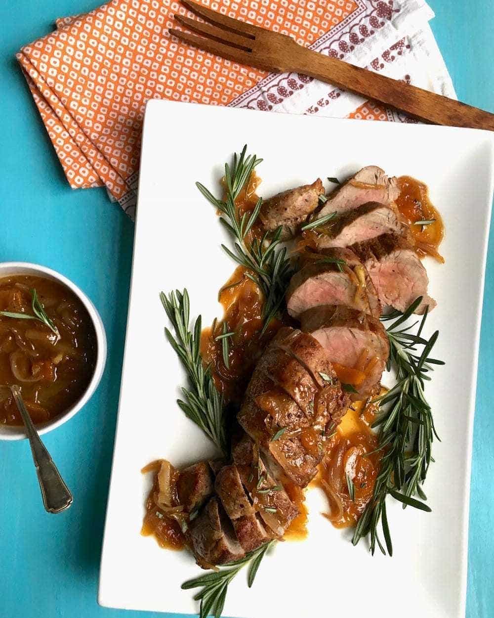 Pork Tenderloin With Rosemary Apricot Sauce on white platter and turquoise background overhead