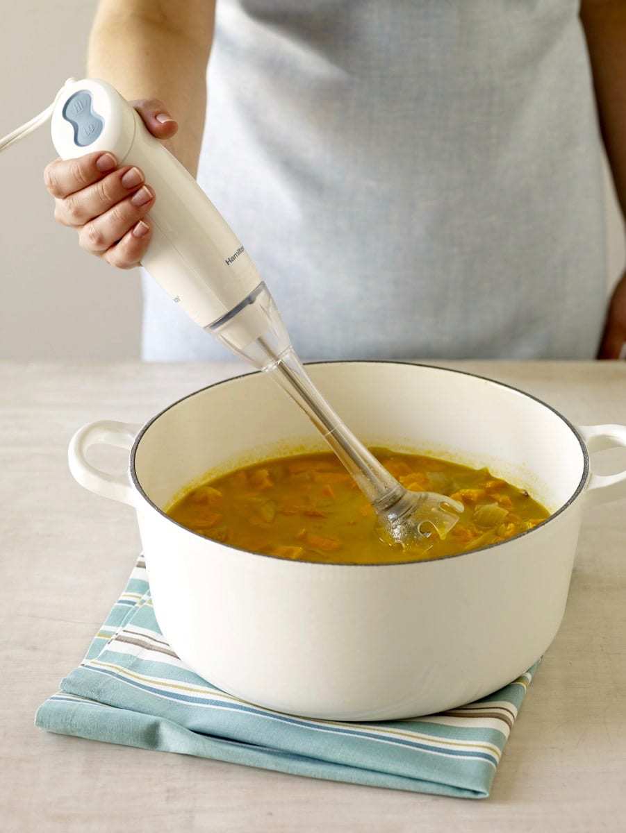 Chipotle Sweet Potato Soup with Queso Blanco in white Le Creueset on striped napkin using an immersion blender.