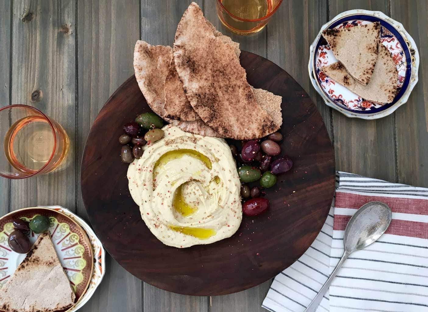 Hummus, olives, naan on wooden plate.