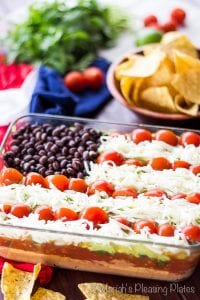 Lightened up 7 layer dip arranged in an American flag pattern with tomatoes, cheese and black beans is a festive addition to your 4th of July food and one of the Tara Teaspoon favorites.