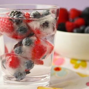 Glass of water filled with ice cubes containing mixed berries